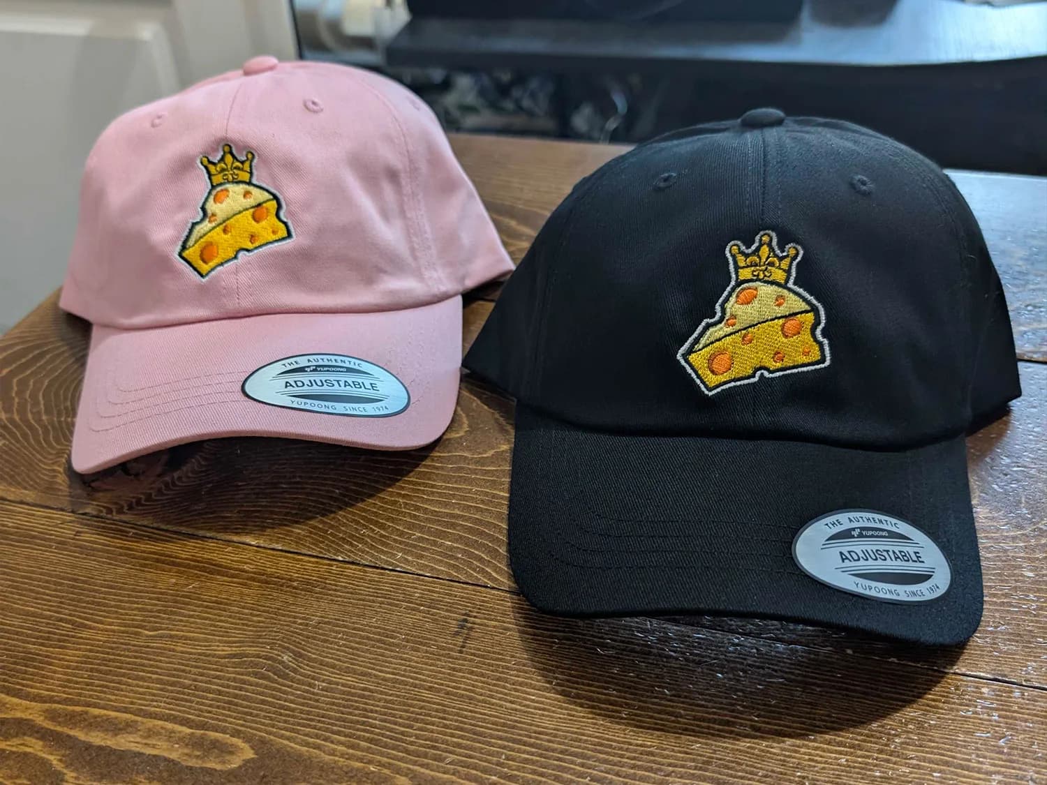 Custom Embroidered Dad Caps Pink and black dad caps with matching yellow crowned cheese logos embroidered on the front.