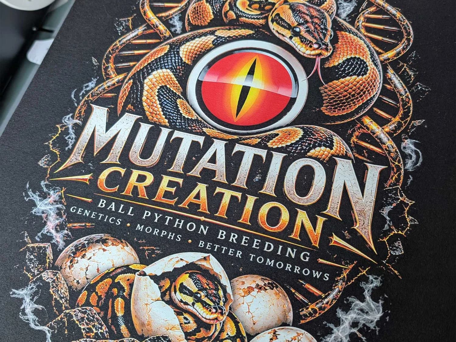 Custom T-Shirt with Full-Colour DTF Printing Black T-shirt with a colourful Mutation Creation print featuring ball pythons, eggs and DNA strands.