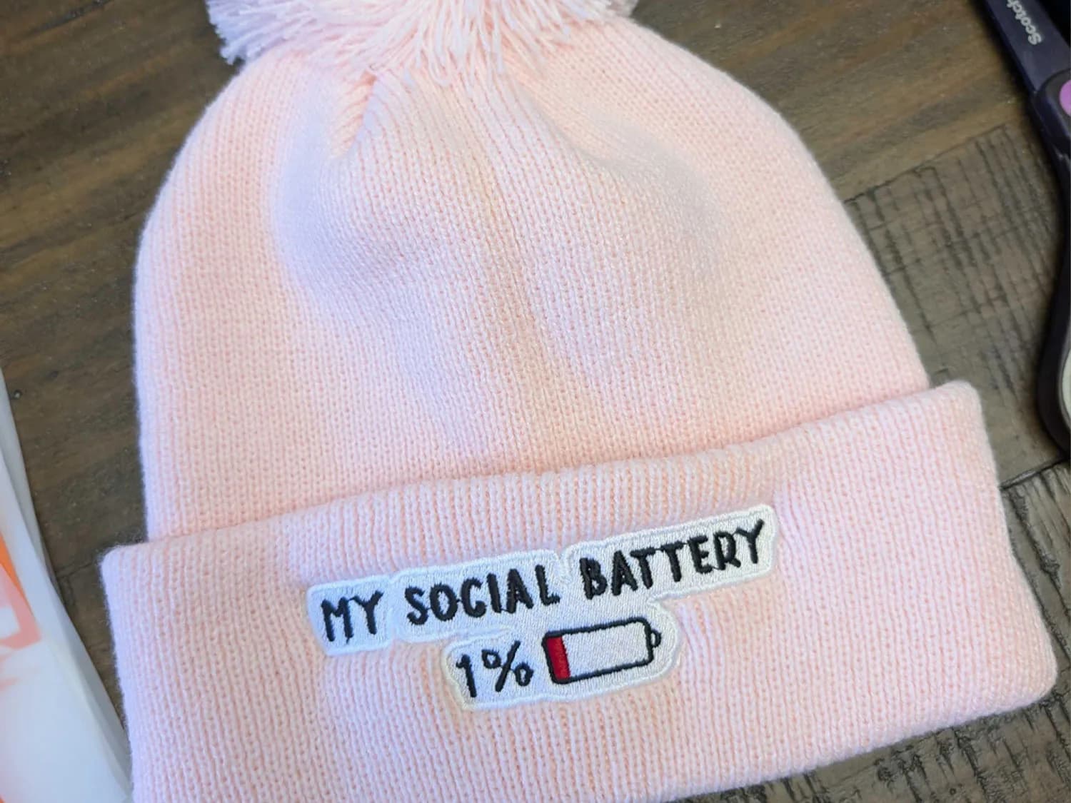 Custom Embroidered Pom-Pom Beanie Pink pom-pom beanie embroidered with “My Social Battery,” “1%” and a nearly empty battery icon.