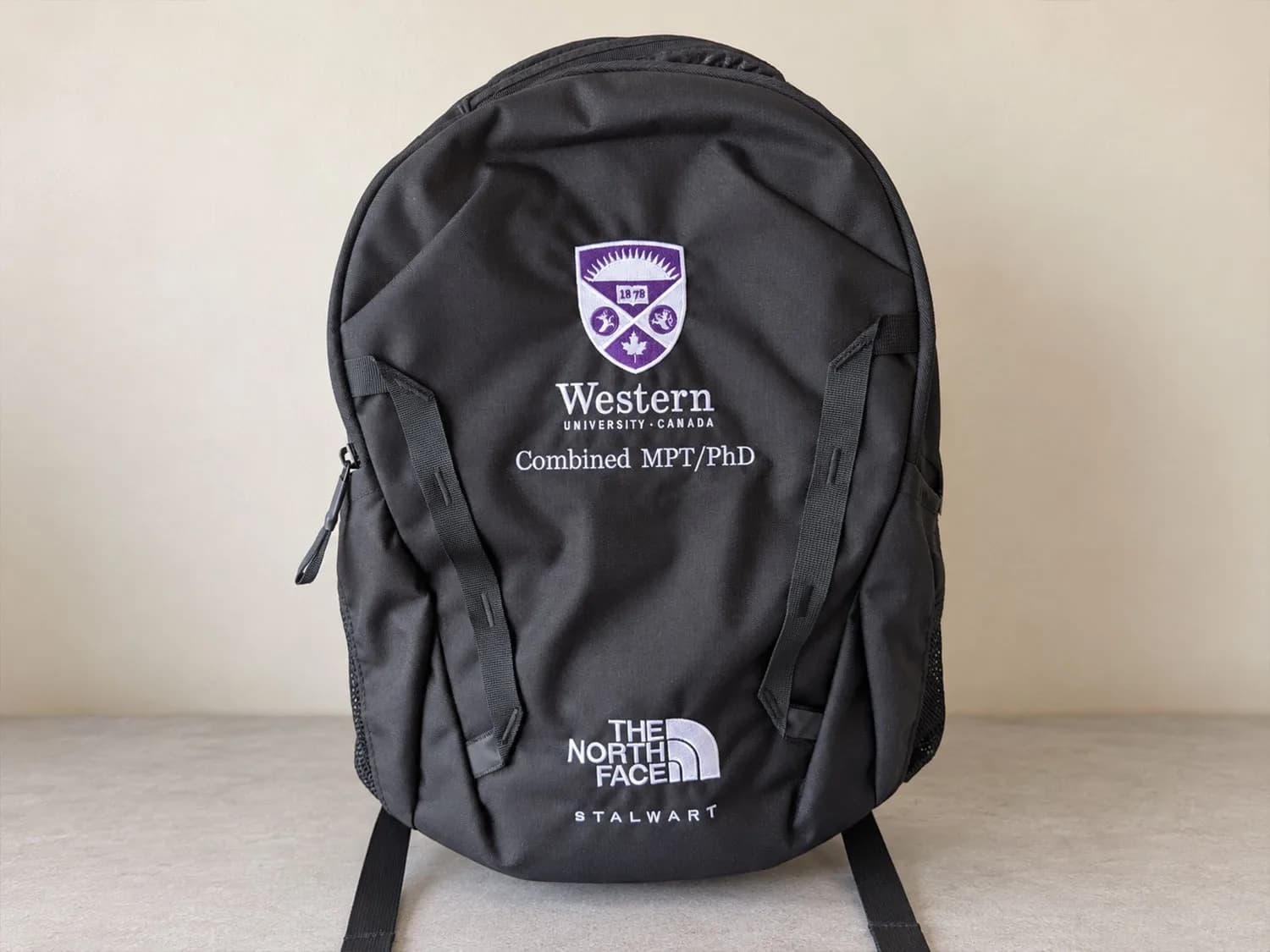 Custom Embroidered North Face Backpack Black North Face backpack embroidered with Western University’s purple and white crest and “Combined MPT/PhD” lettering.