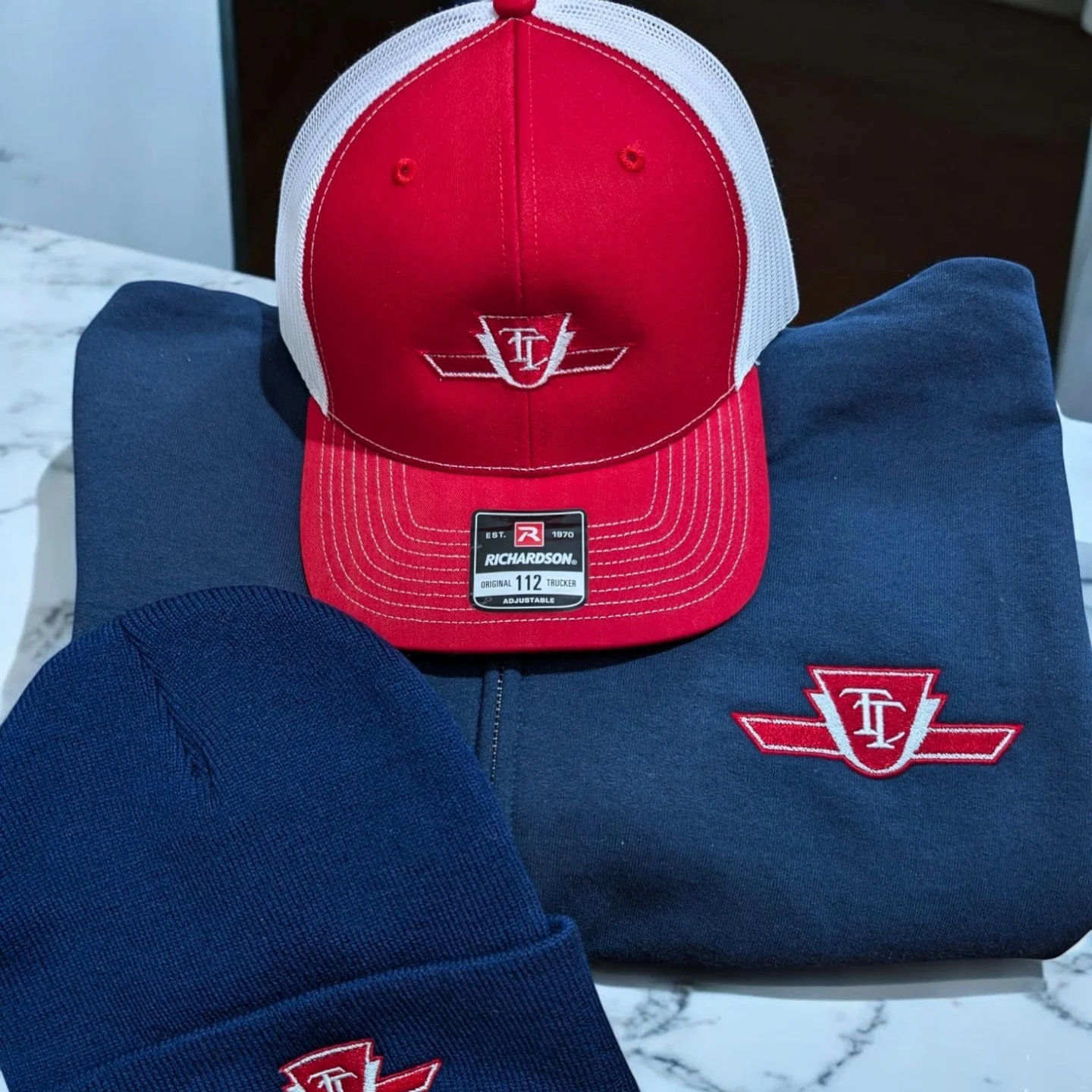 Love the fresh look of our custom apparel pieces! The new red and white logo design really pops on these stylish items - the trucker hat, beanie, and hoodie all look fantastic. Head over to customcaps.ca to create your own personalized gear today!